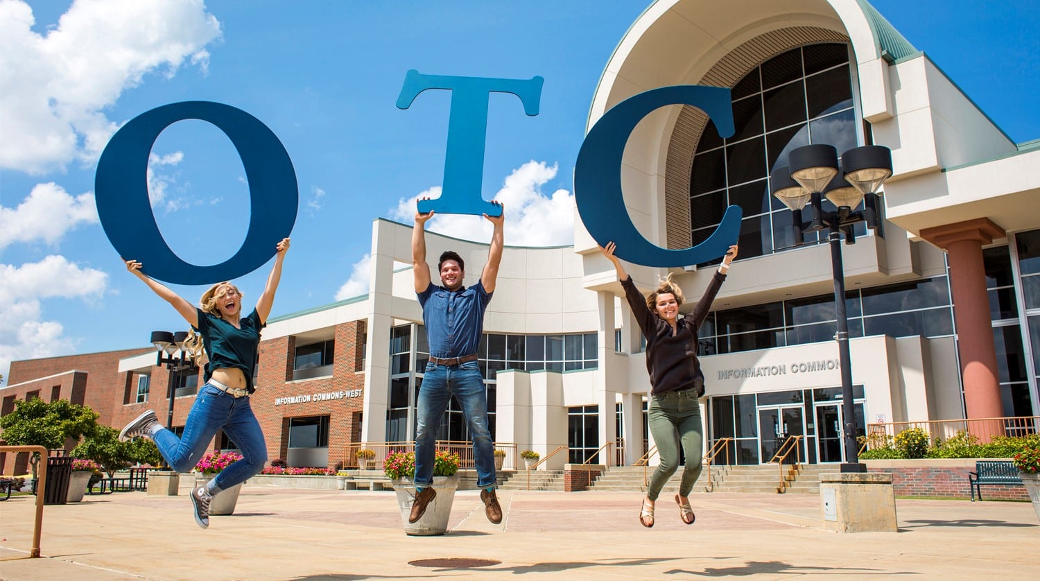 three students jump in the air holding giant OTC letters