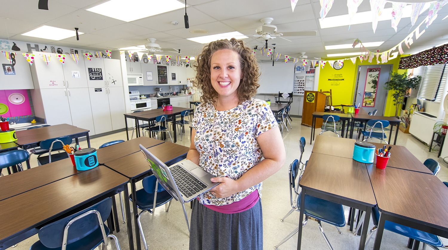 Courtney Dameron stands in her classroom, holding a laptop in her hand.
