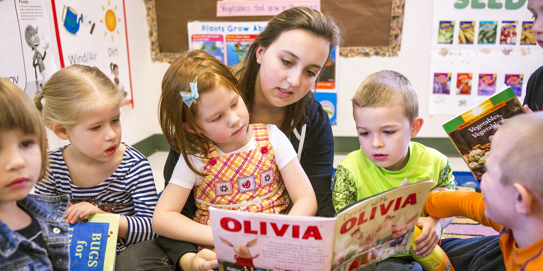 An early childhood teacher and students read a book together