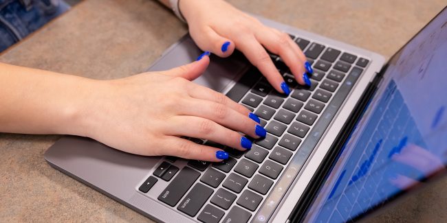 Students in Library and Hallway Sp23 _ 27-full Image of student with blue fingernails typing on a laptop