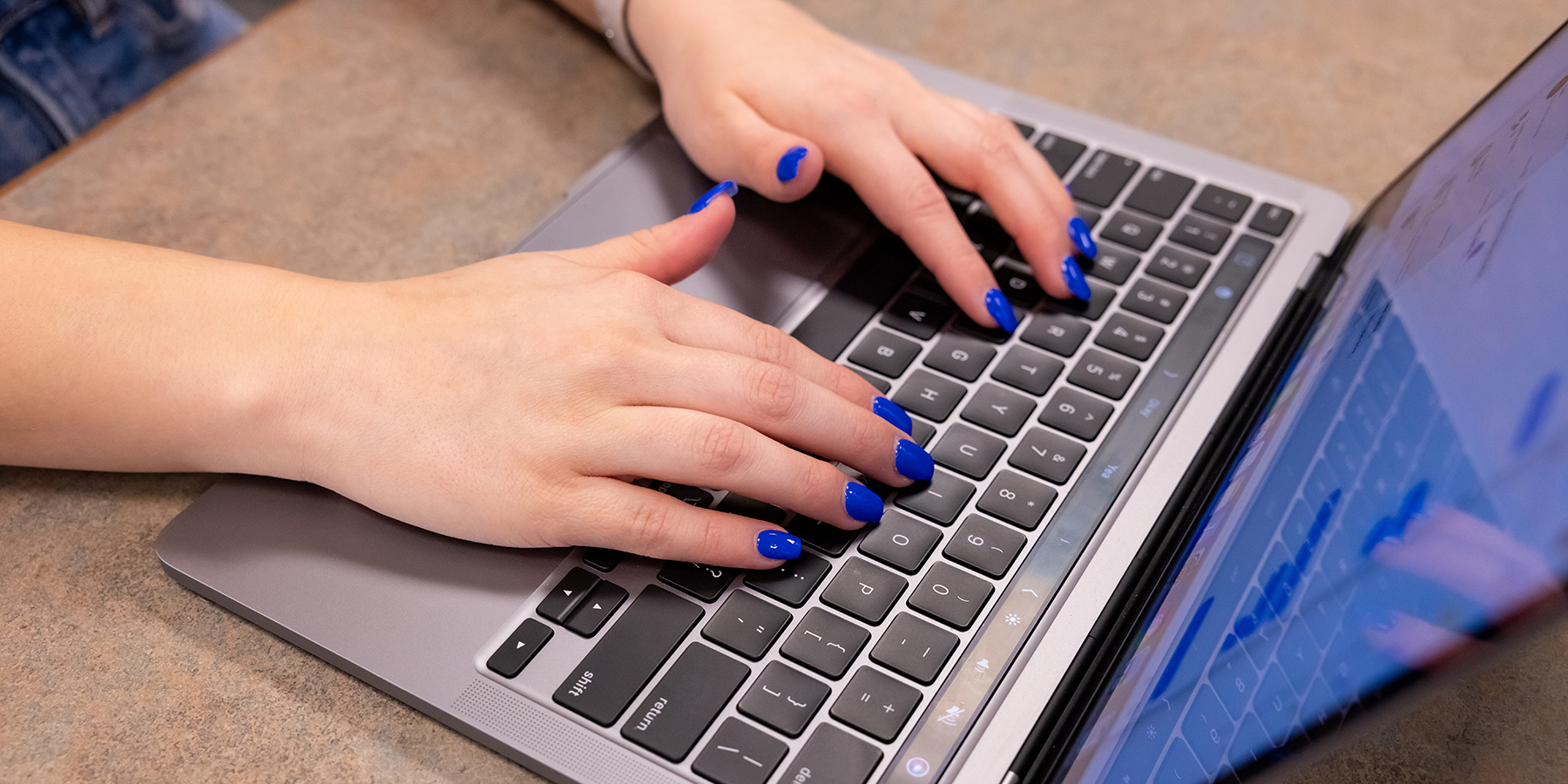 Image of student with blue fingernails typing on a laptop